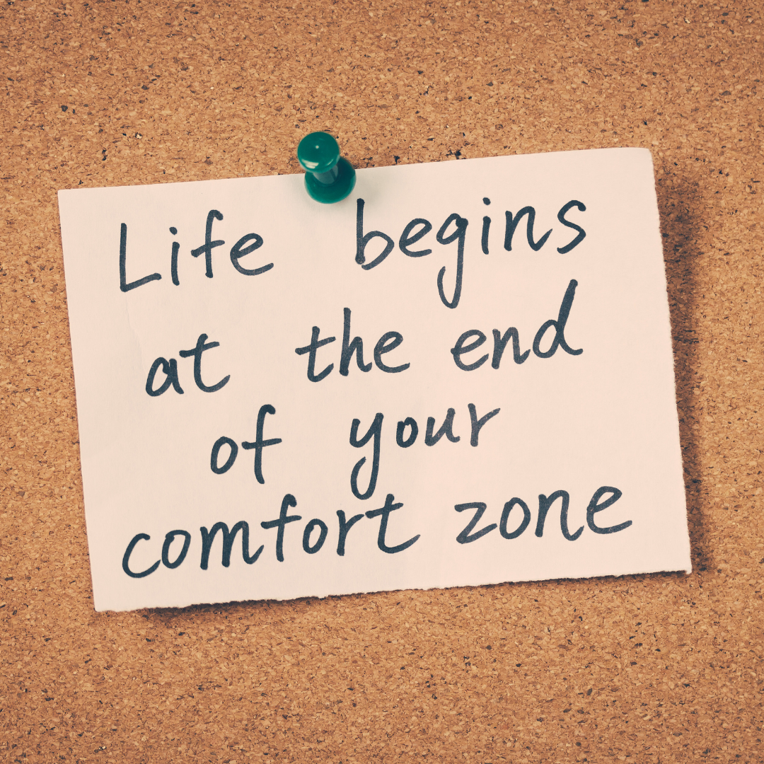 Pinned note that reads "Life begins at the end of your comfort zone" on a corkboard.
